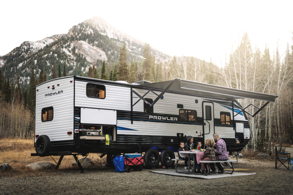 A young family sitting at a picnic table, eating a meal. Behind them, an RV is parked with the awning out.