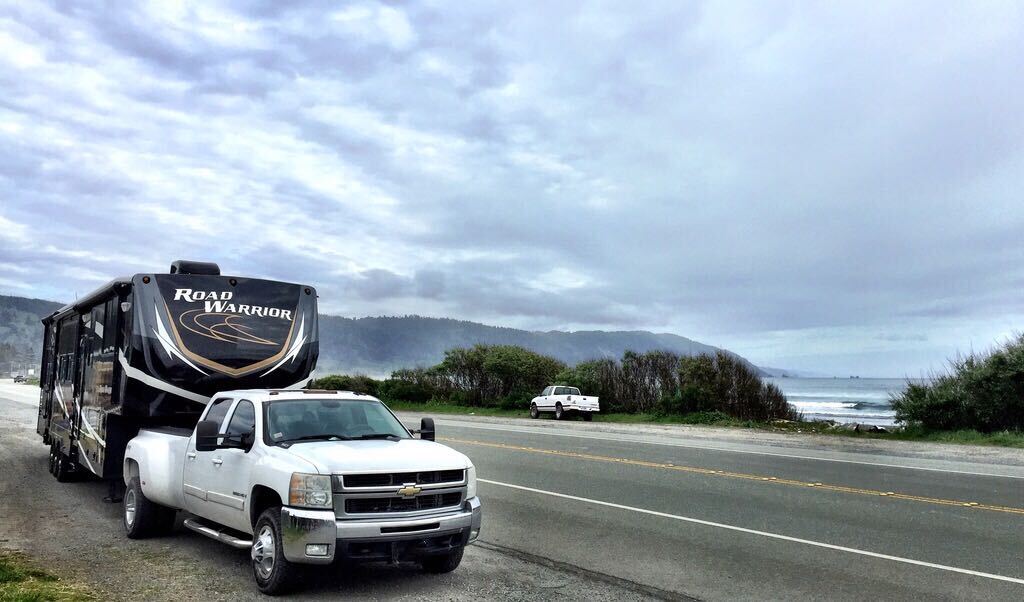 A Heartland Road Warrior RV hitched to a truck by the side of the road on an RV trip.