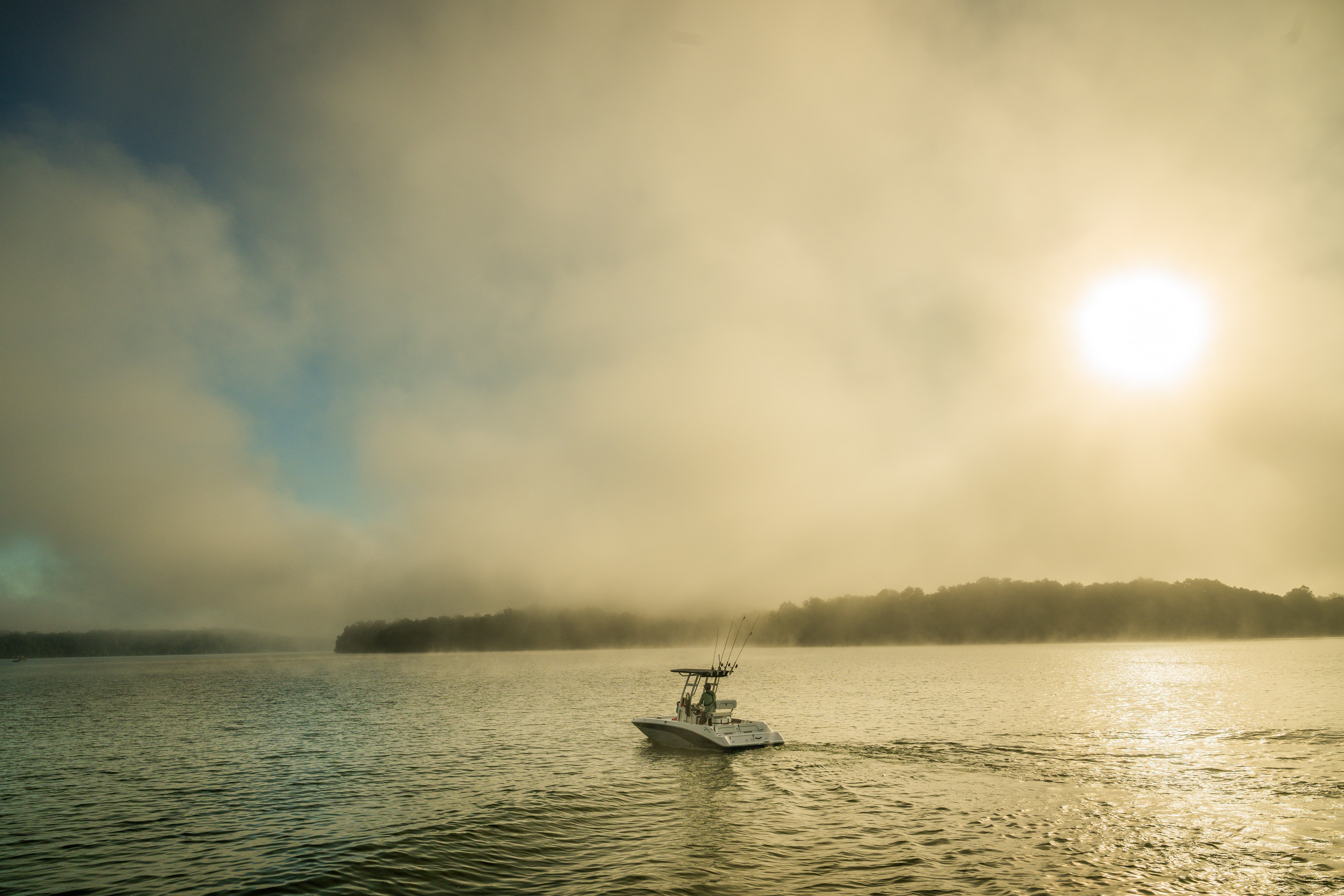 White center console fishing boat with outboard motor traveling on water during sunset with dramatic cloudy sky