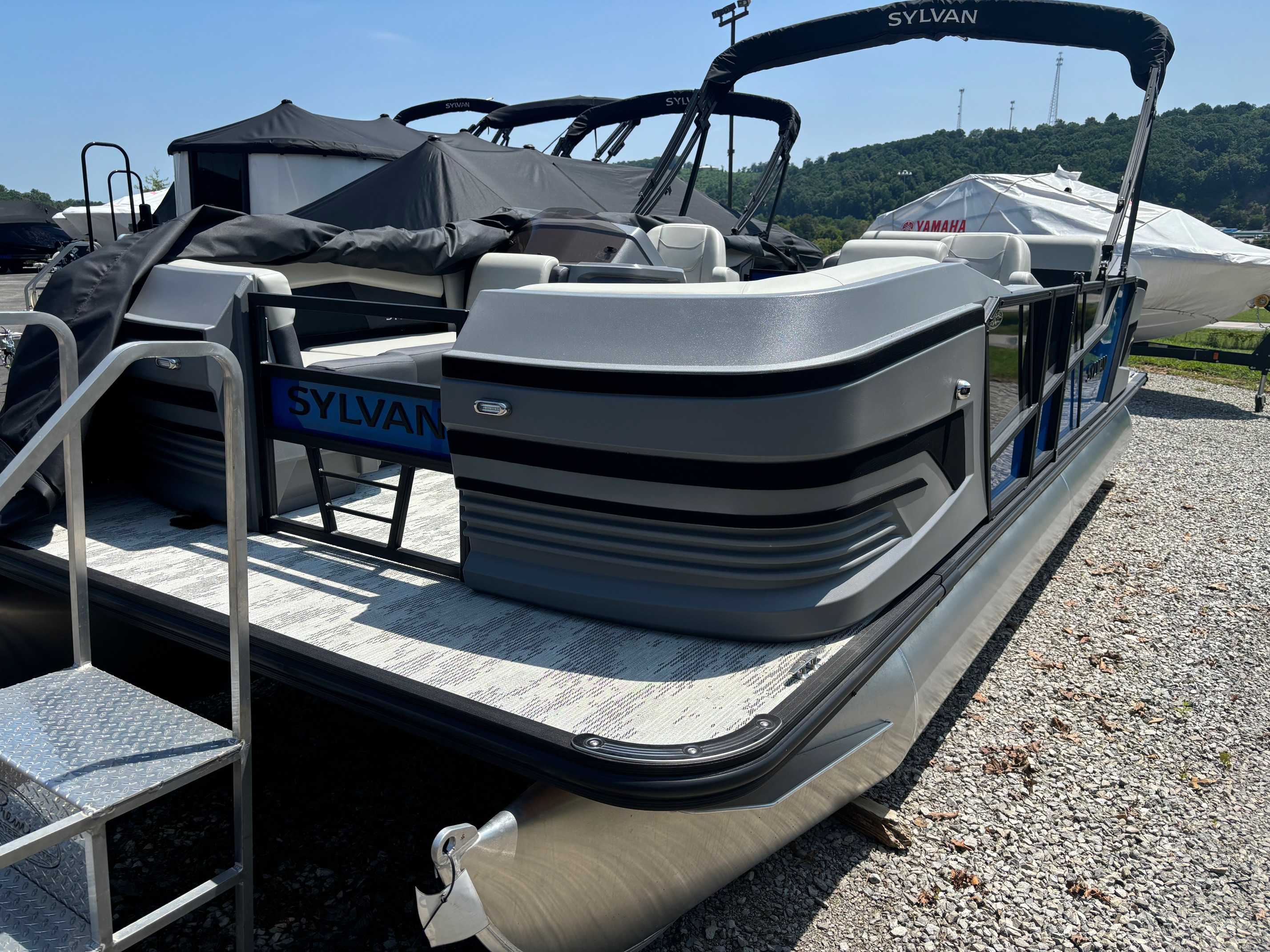 A new 2026 Sylvan R22 CLZ DH pontoon boat, gray in color, is shown on a gravel lot at a dealership.